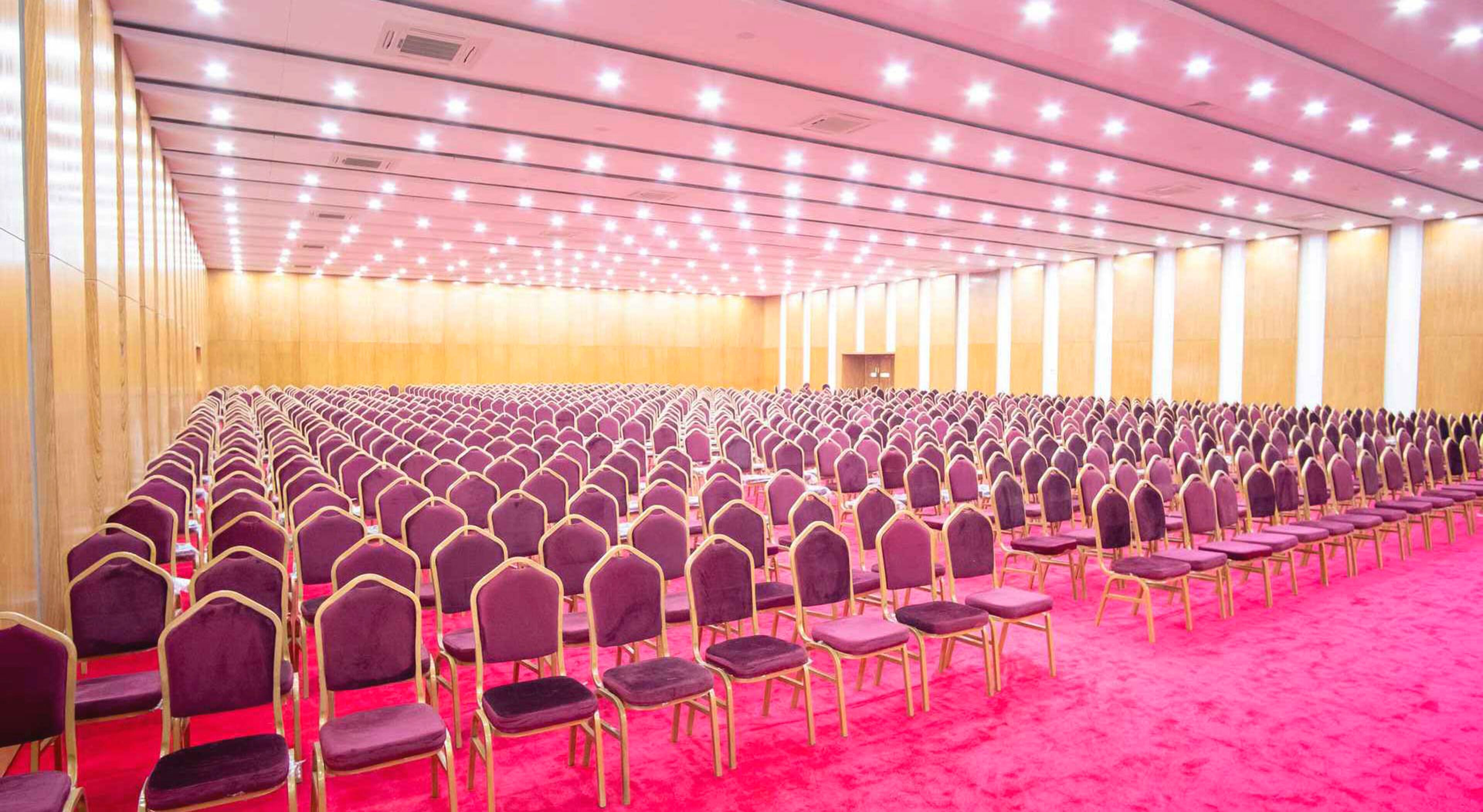 A large conference room with rows of purple chairs and a red carpet.