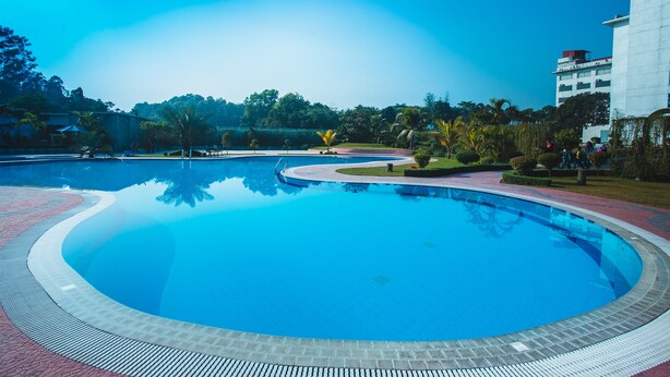 A large, circular swimming pool with a tiled edge, surrounded by a paved walkway and greenery.