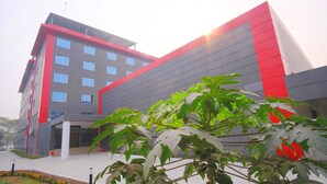 A modern building with a red and grey facade, multiple windows, and a covered entrance area.