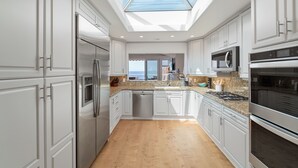 A modern kitchen with white cabinetry, stainless steel appliances, a skylight, and a view to the outside.