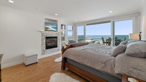 A bedroom with a large bed, a fireplace, and a view of the ocean.