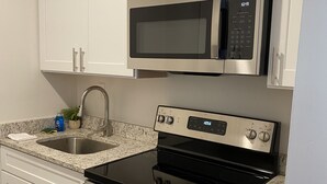 A modern kitchen with white cabinets, a stainless steel microwave, an oven, and a granite countertop. - Innovative Studio Apartment (Gadsden)