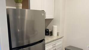 A stainless steel refrigerator, a trash bin, a countertop with a paper towel dispenser, and a potted plant on a shelf. - Innovative Studio Apartment (Gadsden)