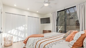A bedroom with a bed, a ceiling fan, a TV, and a sliding glass door.