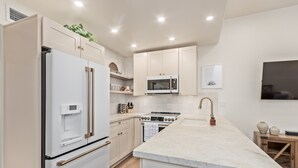 A modern kitchen with white cabinetry, a built-in oven, a microwave, and a stainless steel refrigerator.