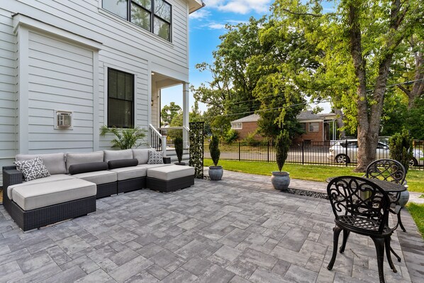 Eine Terrasse mit Ecksofa, Gartenmöbeln und Blumentöpfen.