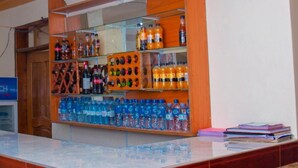 A reception area with a counter, shelves stocked with bottled water and beverages, and a stack of books on the right. - Budget Double Room at Sabunyo Hotel Sironko (Sironko)