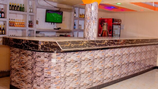 A bar area with a marble counter, shelves with bottles, a television, and a pillar. - Budget Double Room at Sabunyo Hotel Sironko (Sironko)