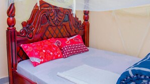 A bed with a wooden headboard, a mosquito net, and red patterned pillows. - Budget Double Room at Sabunyo Hotel Sironko (Sironko)