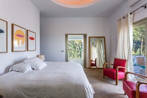 Quarto com cama, uma cadeira vermelha e vista para o exterior.