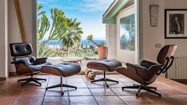 Ein modernes Wohnzimmer mit zwei Ledersofas, einem Couchtisch und Blick auf einen Pool und Grünflächen.