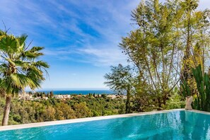 Vista clara de uma piscina, com árvores ao fundo e uma vista distante do mar.