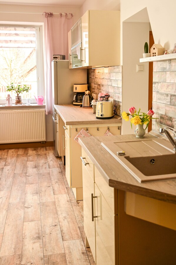 A kitchen with wooden flooring, a toaster, a sink, and a window with a view of trees.