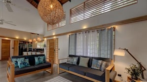 A spacious living area with a large sofa set, a dining table, and a kitchen in the background.
