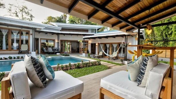A modern outdoor living area with two lounge chairs, a pool, and a covered patio.