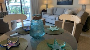 A living room with a round table, two starfish centerpieces, a blue glass vase, and a painting of sailboats on the wall. - Gorgeous 203C Gulf Shores Surf and Racket Club (Gulf Shores)
