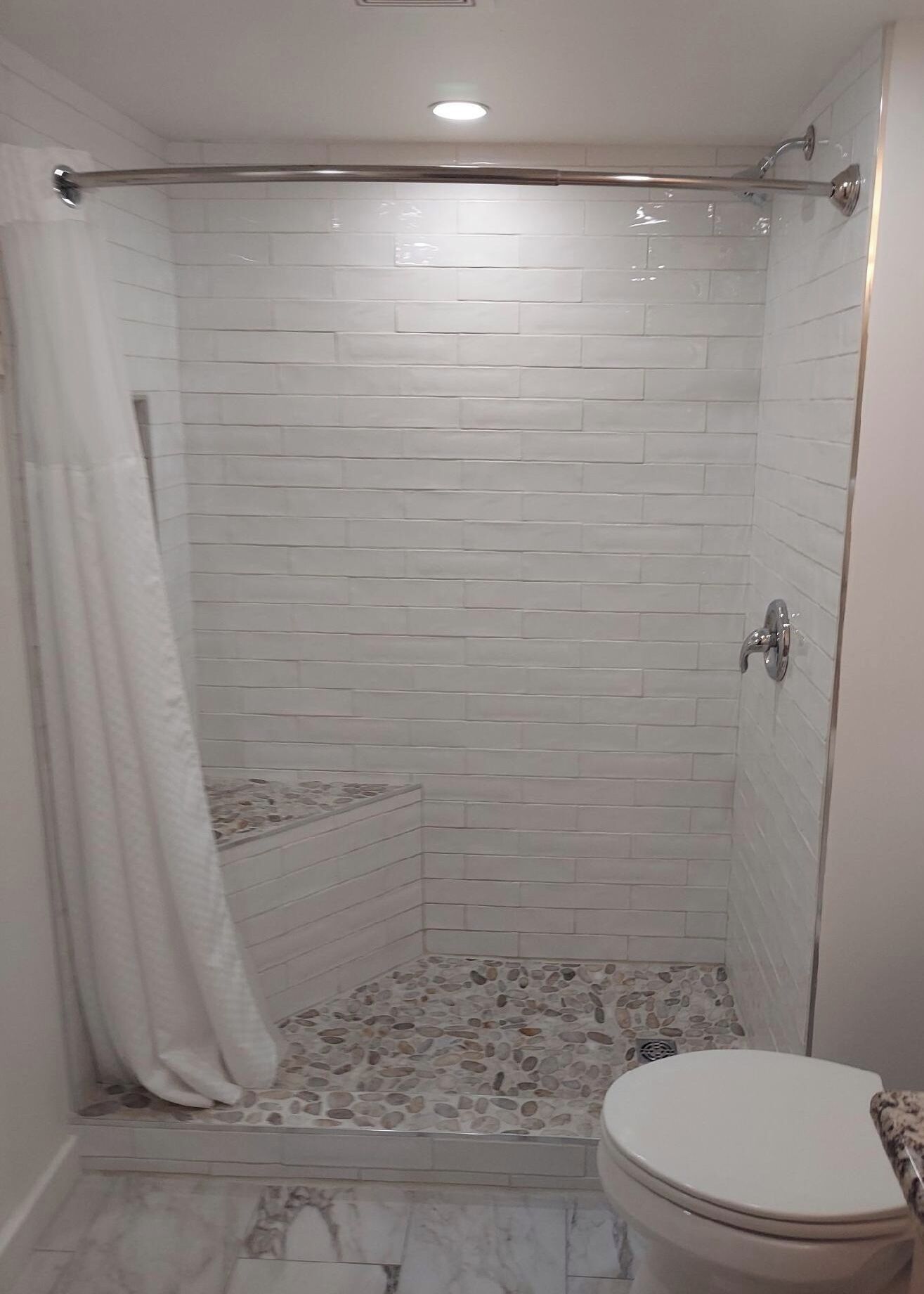Ducha con puerta de vidrio, inodoro blanco y suelo de baldosas.