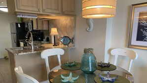 A dining area with a round table, white chairs, a central decorative vase, and a lamp. - Gorgeous 203C Gulf Shores Surf and Racket Club (Gulf Shores)