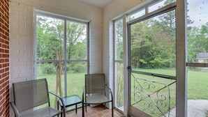A covered patio area with two chairs and a table, large windows, and a view of a grassy yard. - Cozy Tuskegee Home - 20 Mi to Auburn University! (Tuskegee)