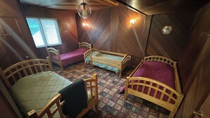 Habitación pequeña con tres camas de madera, piso estampado y ventana con persianas.