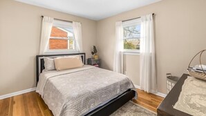 Une chambre à coucher avec un lit, une table de chevet, une fenêtre avec des rideaux et une vue sur un bâtiment en briques à l’extérieur.