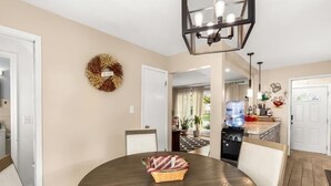 Un coin repas avec une table ronde, des chaises, une couronne décorative et une cuisine en arrière-plan.