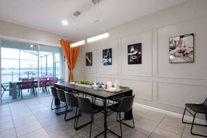 A modern dining area with a long table, black chairs, and a glass partition. - 🌟Themed 12BR 11.5BA Pool Villa / Spa / Close Disney/ 26 PPl  (Kissimmee)