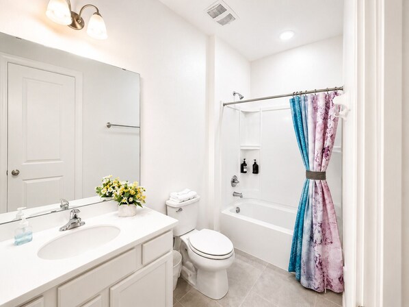 Un baño moderno con lavamanos, inodoro y bañera blancos, cortina de ducha y espejo con luces.