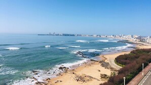 A coastal cityscape with a sandy beach, rocky shoreline, and a clear blue sky. - La P'Tite Case - facing the sea (Les Sables-d´Olonne)