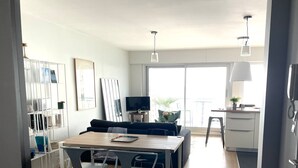 A modern living room with a dining area, a TV, and a balcony with a view. - La P'Tite Case - facing the sea (Les Sables-d´Olonne)