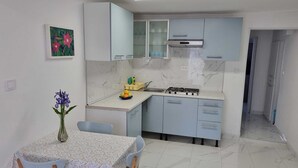 Une cuisine de taille réduite, équipée d’une cuisinière à gaz, d’un évier et de meubles de couleur bleu clair. On y trouve une table à manger avec des chaises et un vase rempli de fleurs.