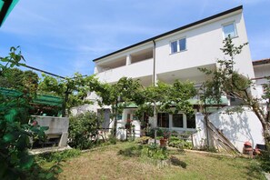 Ein zweistöckiges Gebäude mit flachem Dach, einem Balkon im oberen Stockwerk und einem kleinen Garten davor.