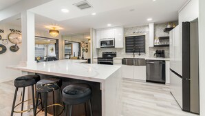 A modern kitchen with a central island, bar stools, stainless steel appliances, and decorative wall clocks. - Blackrock Lux ~ High-End Designer Oasis ~ 7min from Airport ~ EV Charger (Fort Lauderdale)