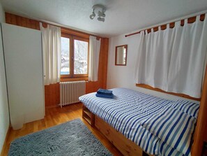 A bedroom with a wooden bed, a window with curtains, a radiator, and a mirror on the wall.