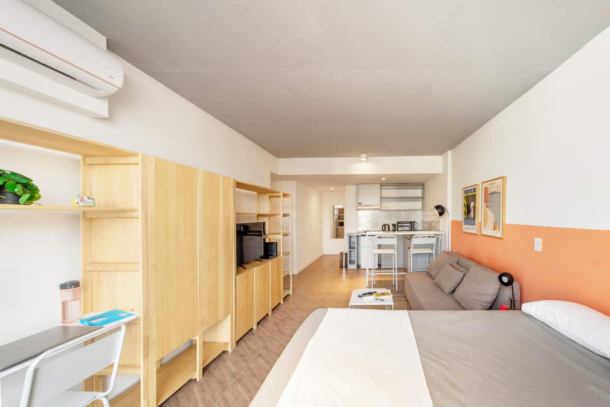 A compact hotel room with a kitchenette, a bed, a desk, and a sofa.