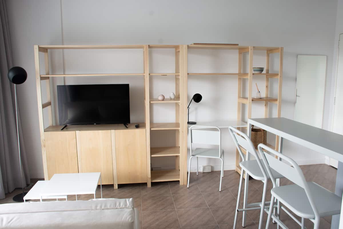 A modern living room with a TV, white furniture, and wooden shelves.