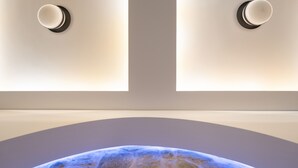 A modern room with a large, curved wall-mounted globe and two wall sconces. - SARTORI CONCEPT HOTEL (Heraklion)