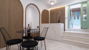 A modern interior with a dining area featuring a round table and four chairs, a reception desk, and a staircase leading to an upper level. - SARTORI CONCEPT HOTEL (Heraklion)