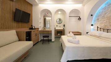 Una habitación de hotel moderna con sofá, cama con toallas, escritorio con silla, televisión y baño con espejo.