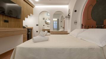 Une chambre d’hôtel moderne, dotée d’un grand lit, d’un téléviseur fixé au mur et d’une salle de bain visible à travers une porte en arc de cercle.