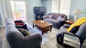 A living room with a sofa, armchair, coffee table, and TV. - Carolina Rose - Steps from the Beach in Oceanside Village (Surfside Beach)