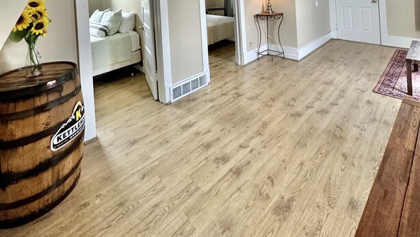 A spacious living area with a wooden floor, a white door, and a small table with a lamp.