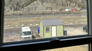 A view through a window of a building with a green shed, a white van, and a red building in the distance.