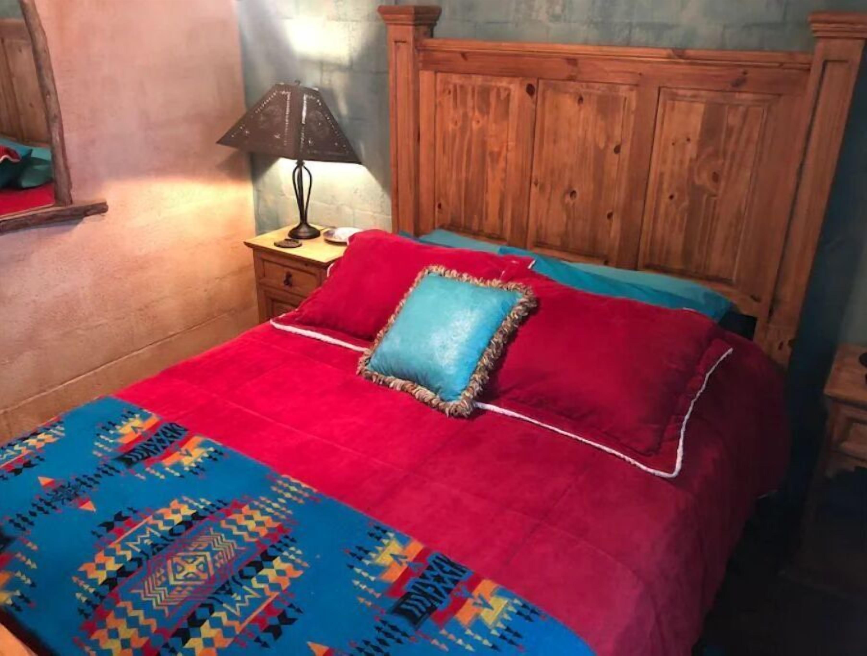 A bed with a red and blue bedspread, a wooden headboard, and a nightstand with a lamp.