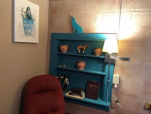 Ein türkisnes Regal mit Dekoration, ein roter Sessel und eine Wandlampe.