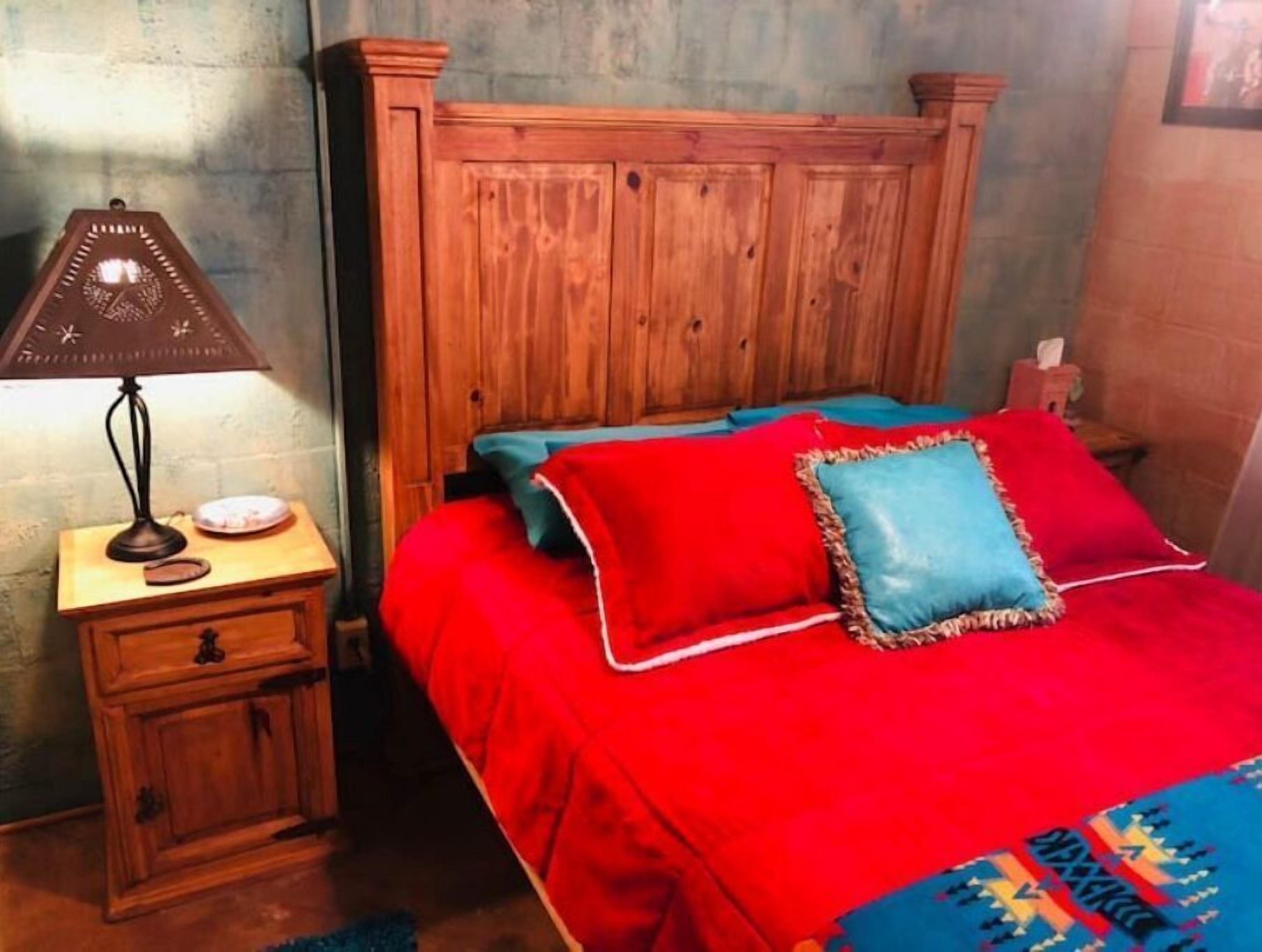 A room with a wooden headboard bed, a nightstand with a lamp, and a small cabinet.