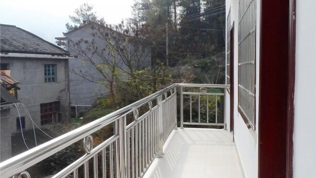 En balkon med gelænder i metal, flisegulv og udsigt til bygninger og træer i det omkringliggende område.