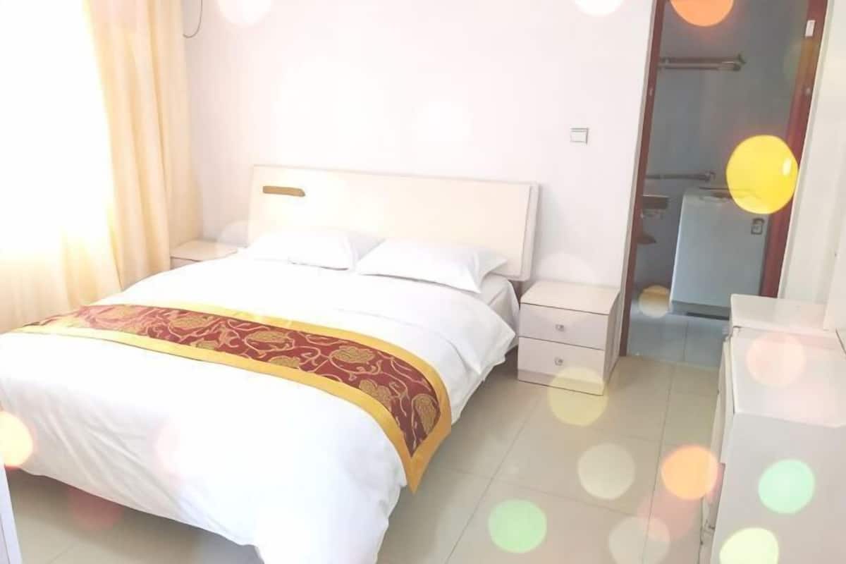 A bed with a white headboard, a red and gold bedspread, and a nightstand with a lamp.