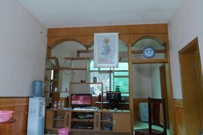 A room with a wooden desk, a computer, and a chair. There is a window with a view of trees. - Caiyin Inn (Zhangjiajie)