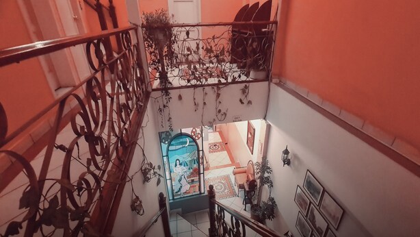 A staircase with ornate metal railings, a door with a decorative glass panel, and a tiled floor leading to a room with a patterned rug and a chair. - Hotel Chat Noir Cuenca (Cuenca)